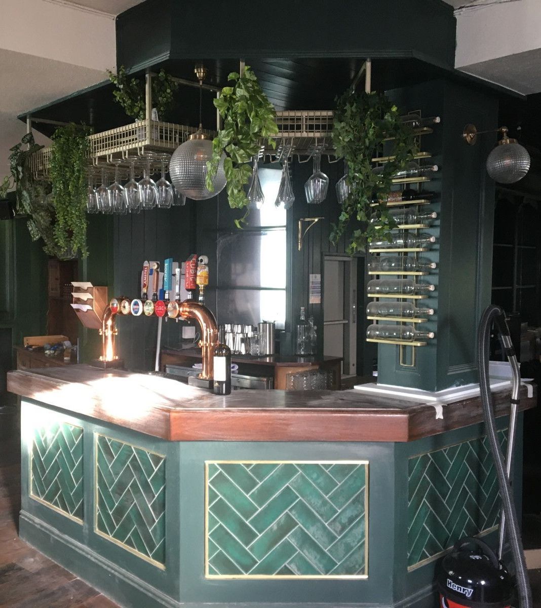 A bar in a restaurant with green tiles and a vacuum cleaner.