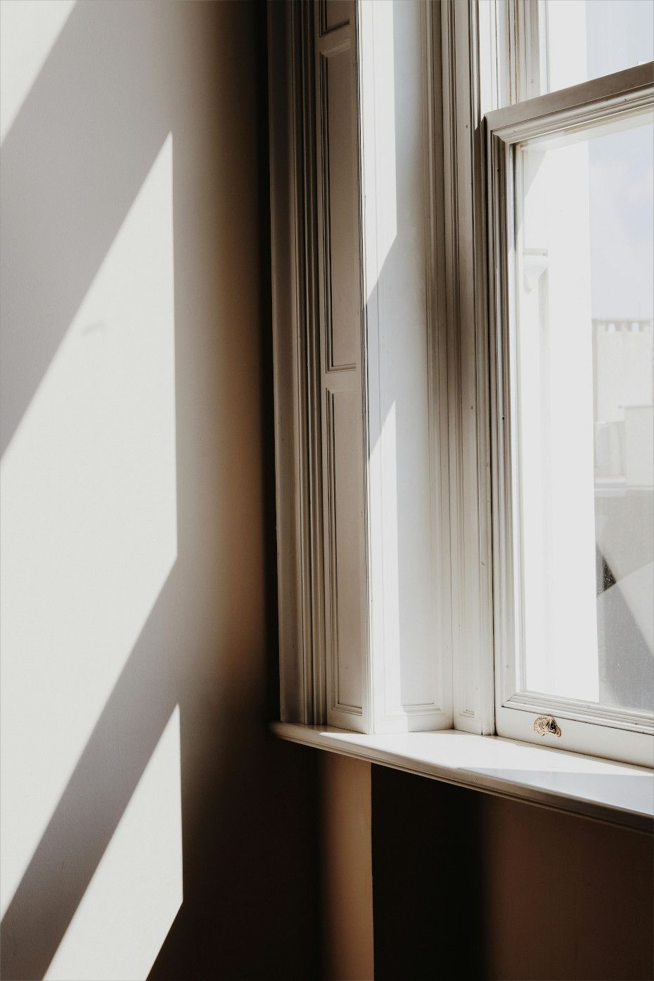 Sunlight streams through a white window, casting shadows on a wall.
