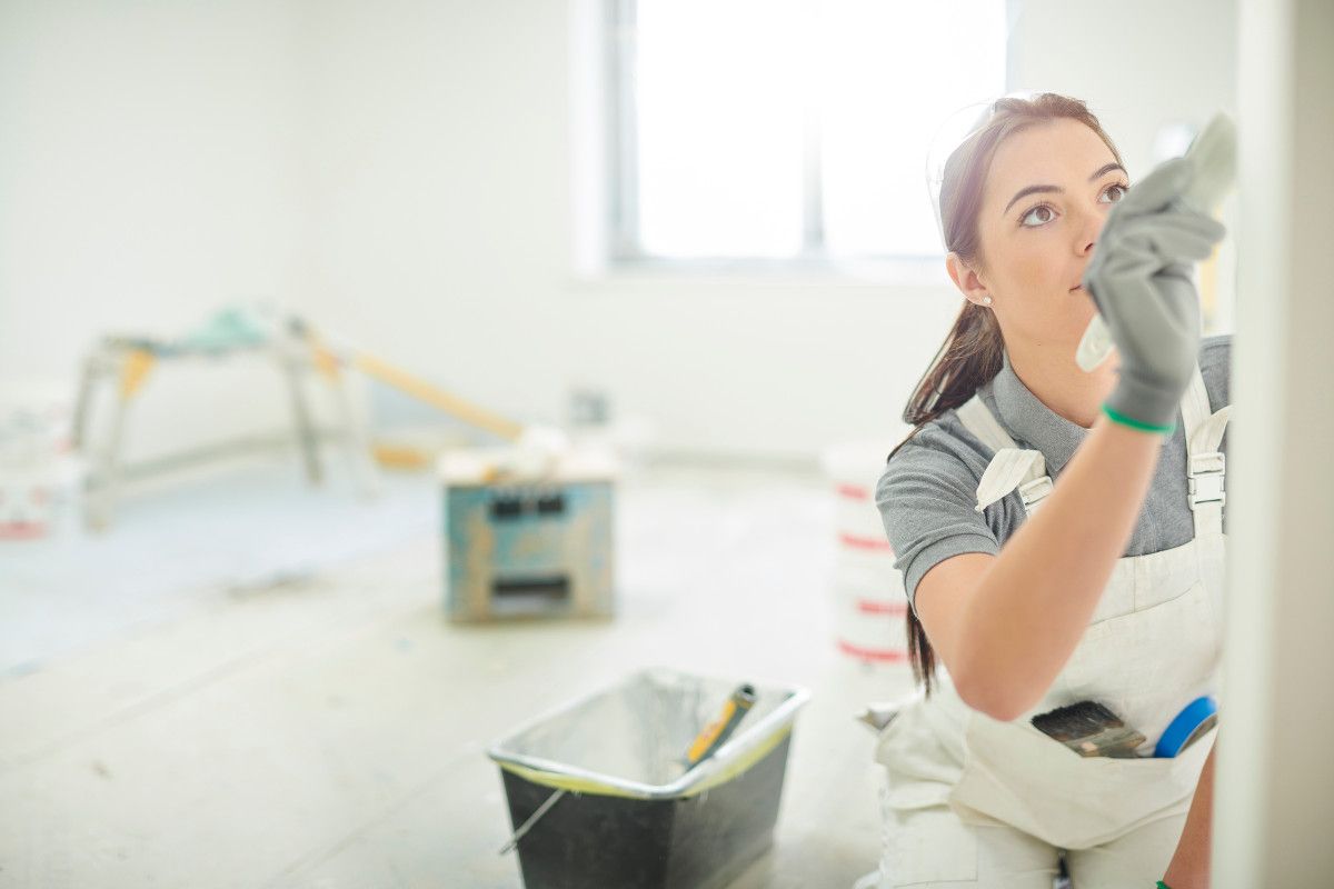 Expert Swansea female painter, applying careful brushstrokes to a wall in a blank room with decorating tools by Daffodil Decor.