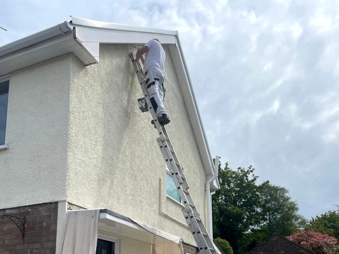 Expert house exterior painter from Daffodil Decor on a ladder painting the exterior of a house as part of a property refurbishment.