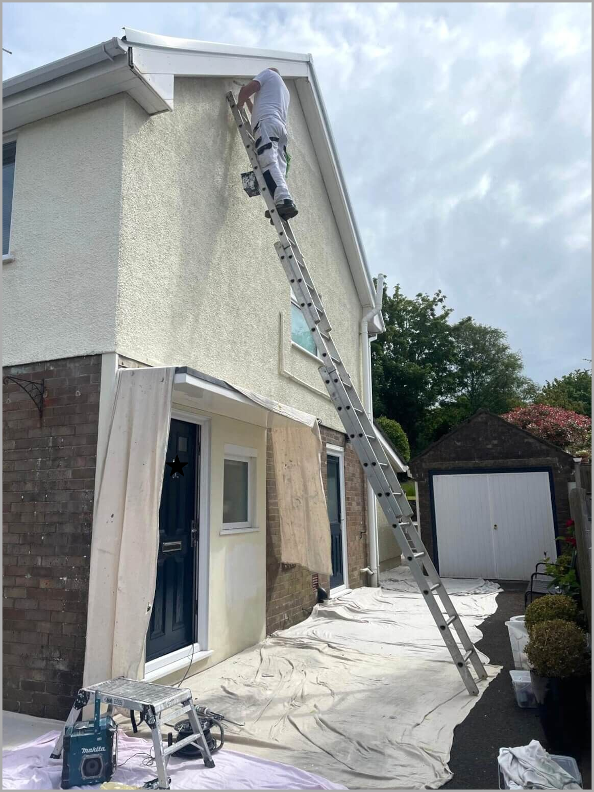 Exterior wall painter at work on a ladder decorating a Swansea house render pebbledash wall by Daffodil Decor.