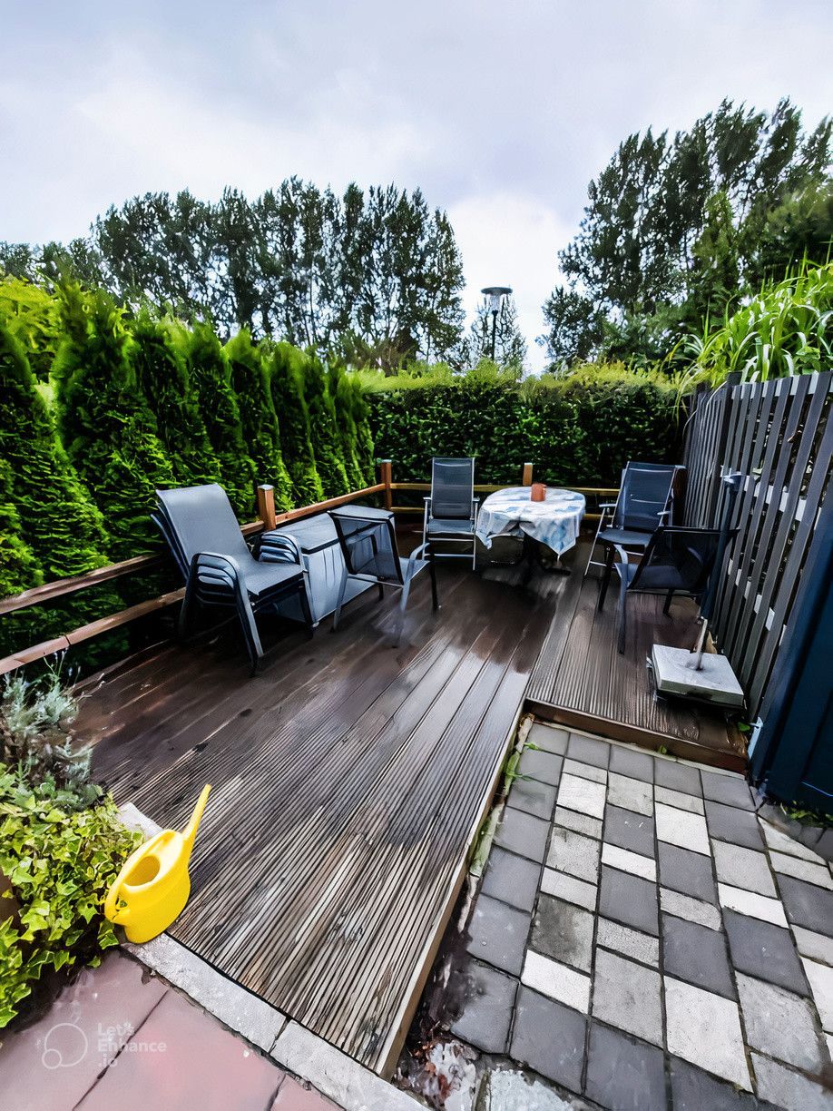 A patio with a wooden deck , chairs , a table and a watering can.