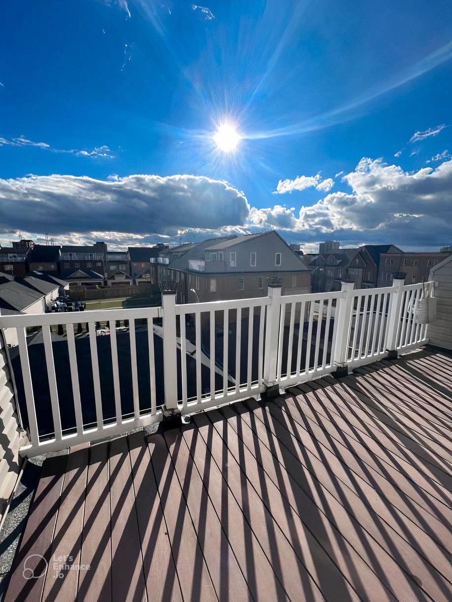 A balcony with a white railing and the sun shining through the clouds