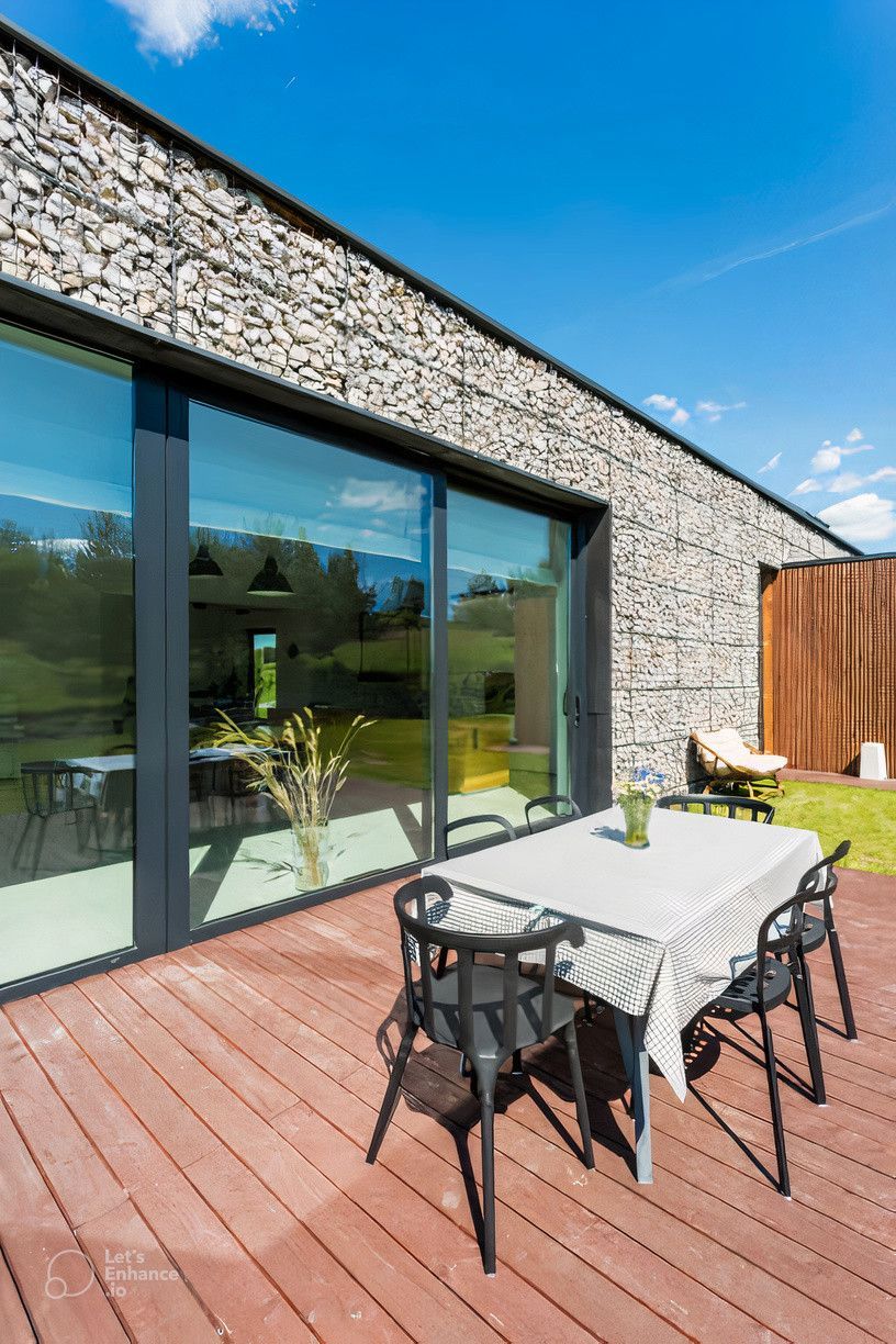 There is a table and chairs on the deck in front of a house.