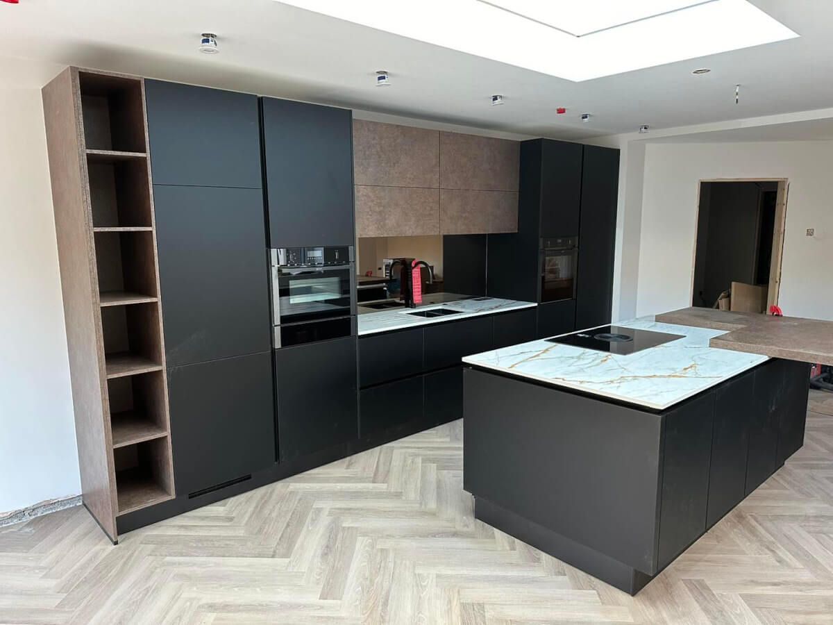 Modern kitchen with dark cabinets, island with stovetop, and herringbone floor. House refurbishment in Swansea.