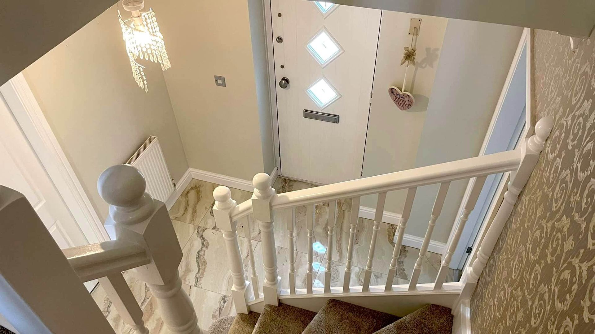 Looking down a white staircase towards a front door with diamond-shaped windows and a hanging decoration. Painted interior of a Mumbles home by Daffodil Decor.