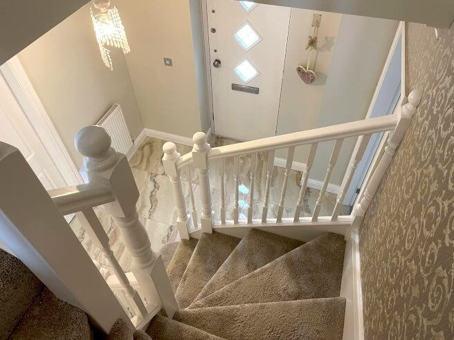 Looking down a white staircase towards a front door with diamond-shaped windows and a hanging decoration. Painted interior of a Mumbles home by Daffodil Decor.