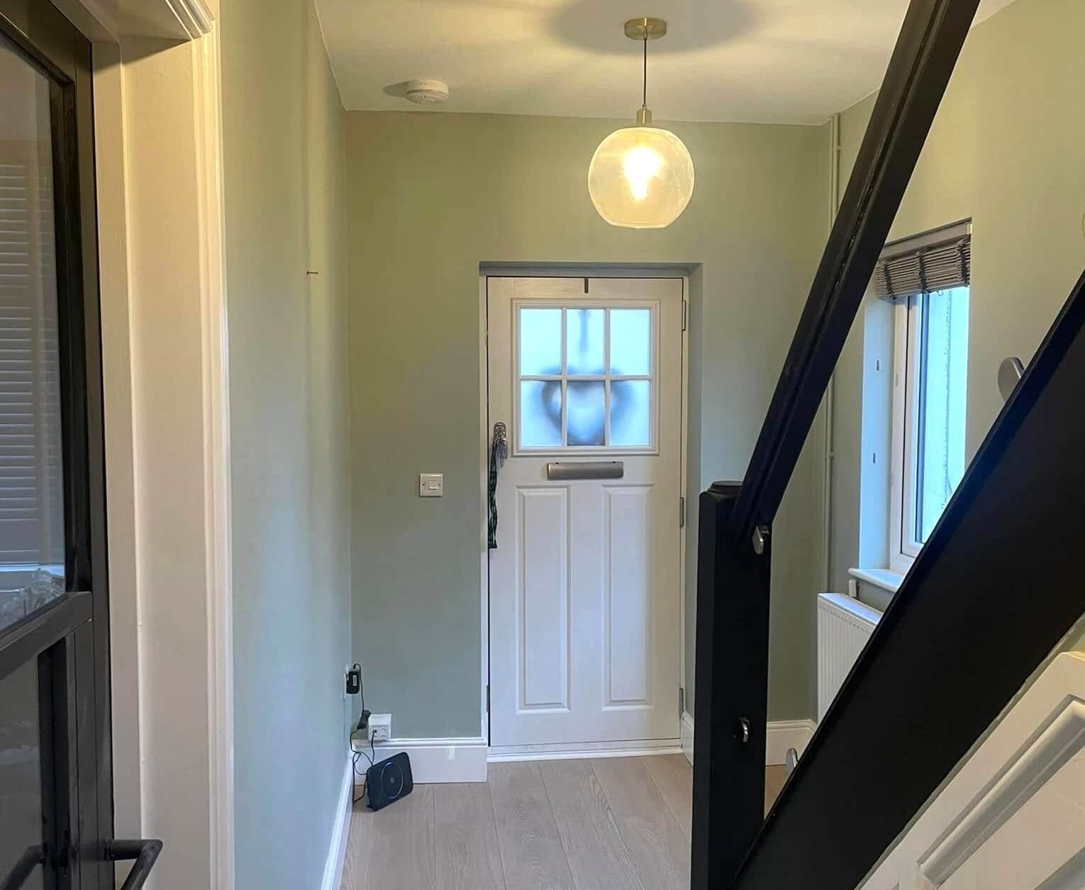 Entryway with sage green walls, white door with frosted glass, and hanging globe light. Swansea hallway painted by Daffodil Decor.