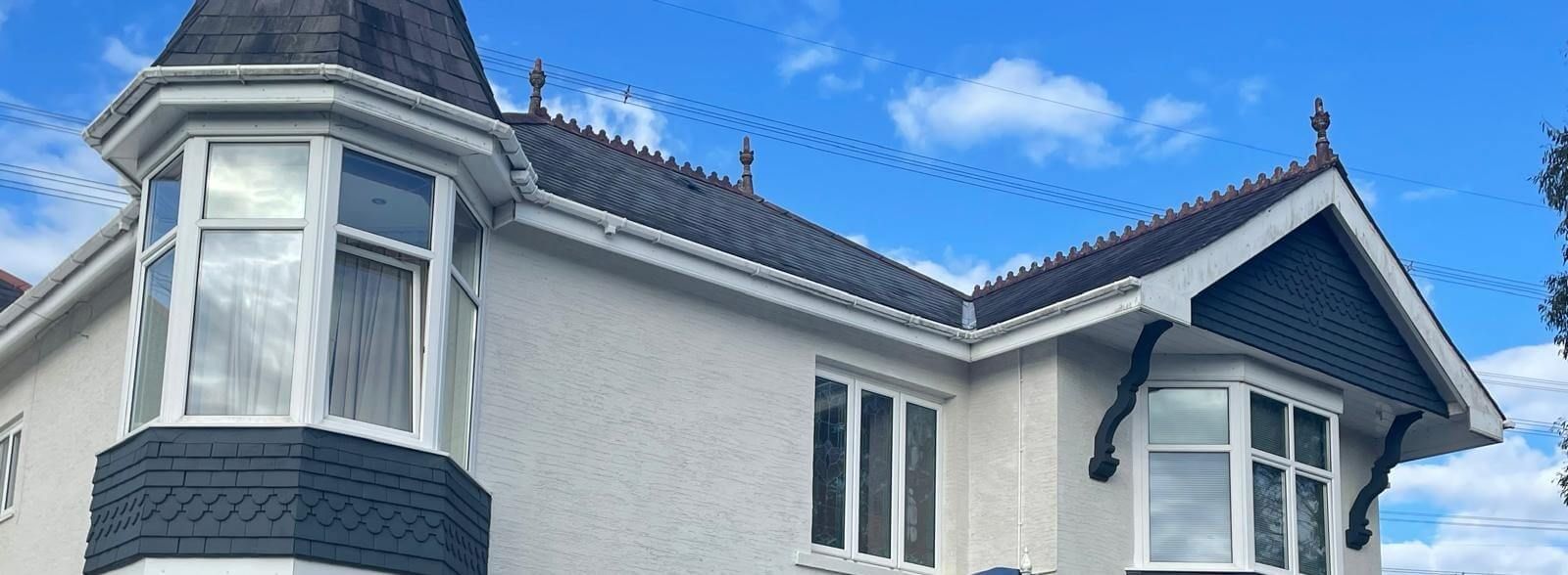 White Swansea house with dark trim and a turret against a blue sky with clouds. Exterior painted by Daffodil Decor.