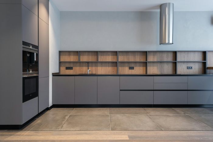 A modern kitchen with gray cabinets and wooden shelves.