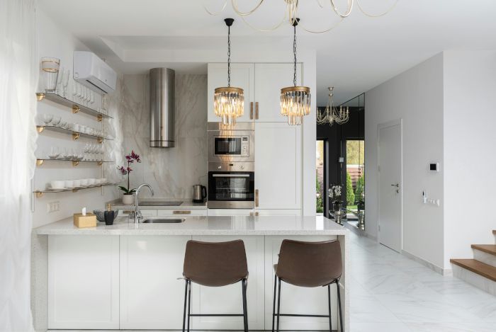 A kitchen with white cabinets , stools , a sink and a refrigerator.