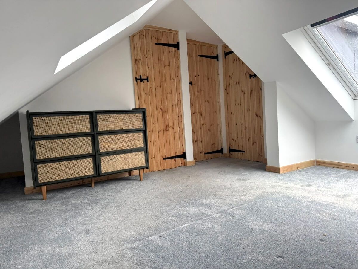 Attic room with sloped ceiling, carpet flooring, wooden closet doors, and dresser. Decorated by Daffodil Decor in Swansea during home renovation.