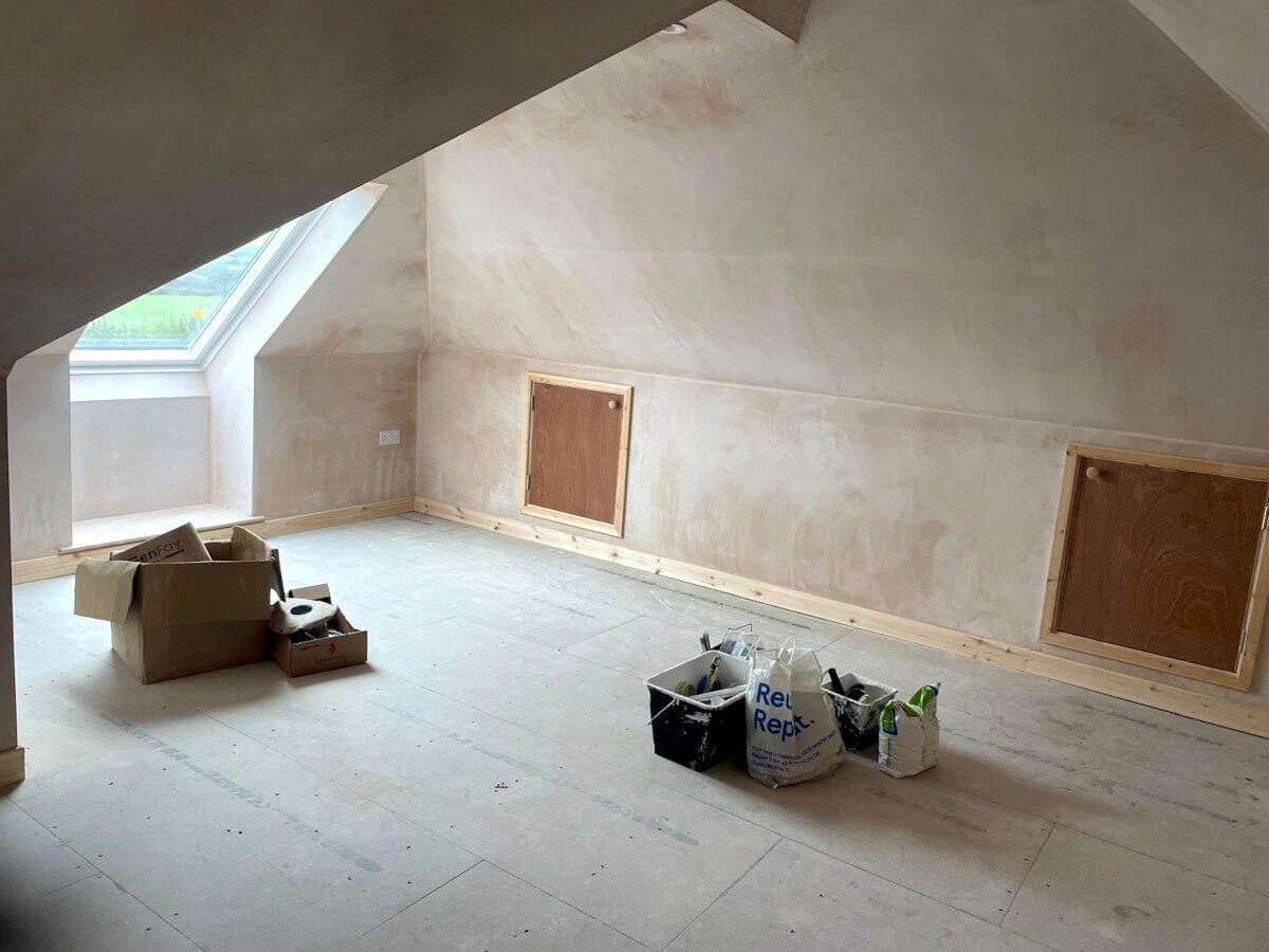 Attic room under construction with sloped ceiling, skylight, bare wood floor, and plaster walls. House refurbishment in Swansea by Daffodil Decor.