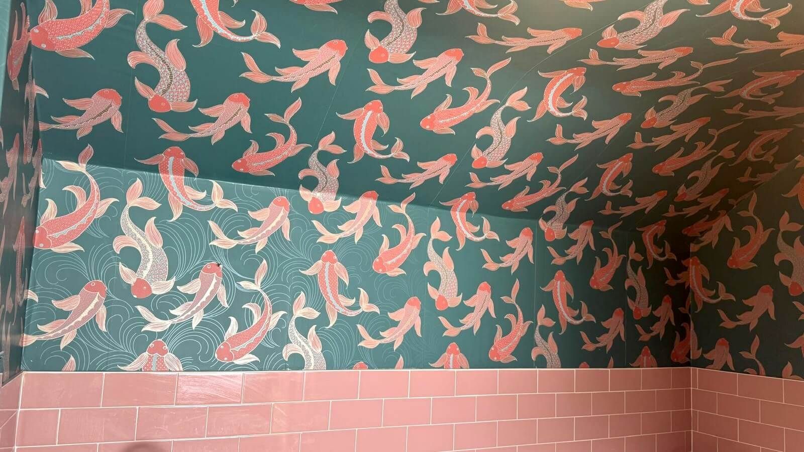Green and salmon fish wallpaper in a bathroom with pink tiled lower walls.