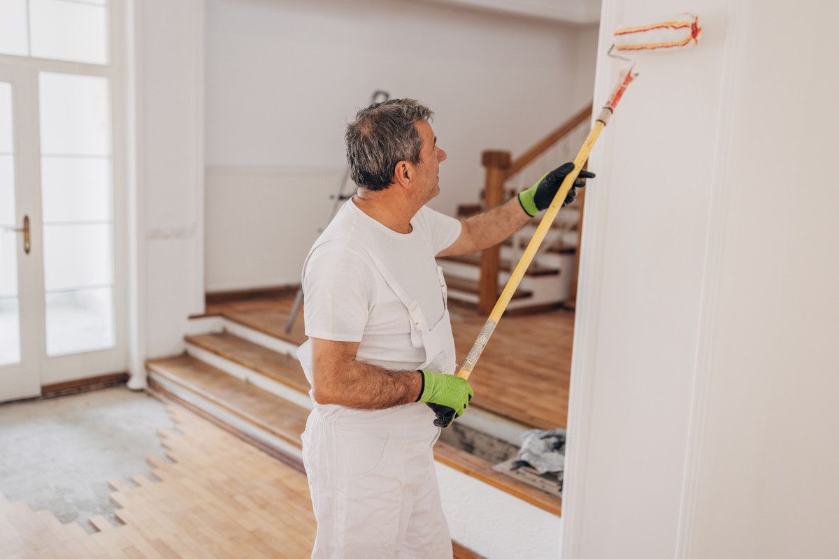 Daffodil Decor painter decorating a white wall with a roller, wearing white clothes and green gloves, interior setting in Swansea.