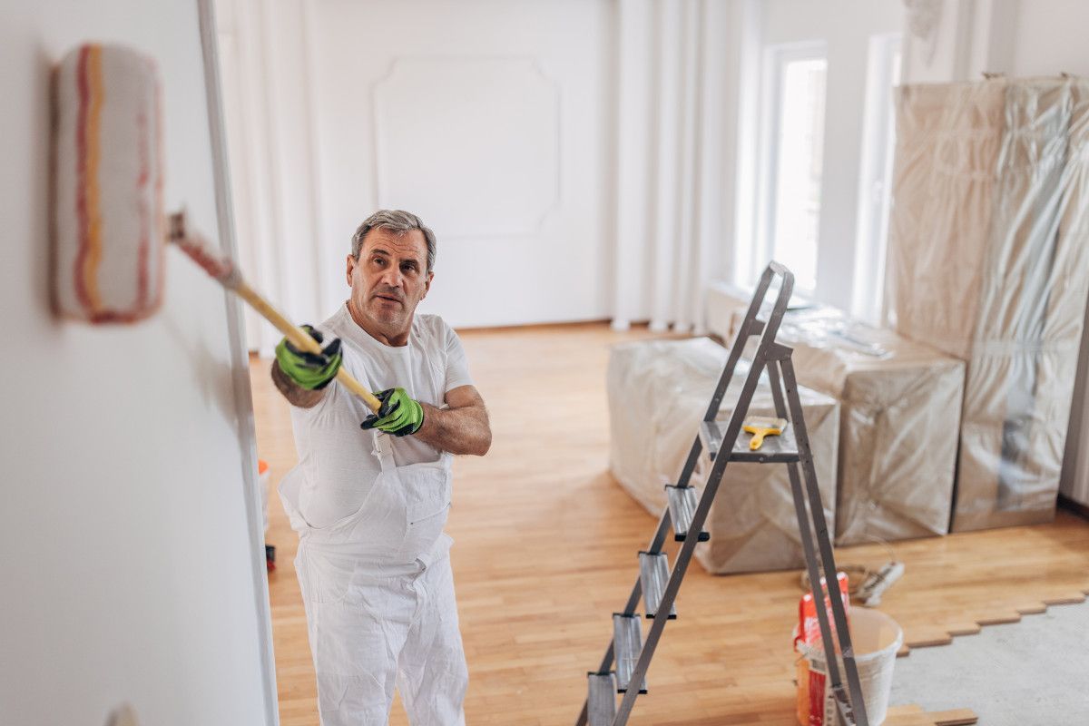 Swansea painter from Daffodil Decor in white overalls uses a roller to apply paint to a wall, ladder nearby.