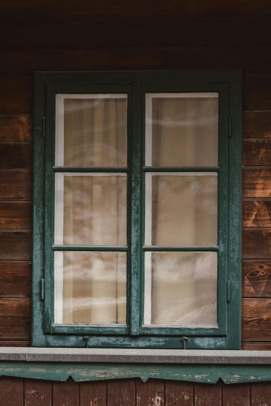 Green-framed window with six panes on a wood-paneled wall. Faint white curtains visible inside.