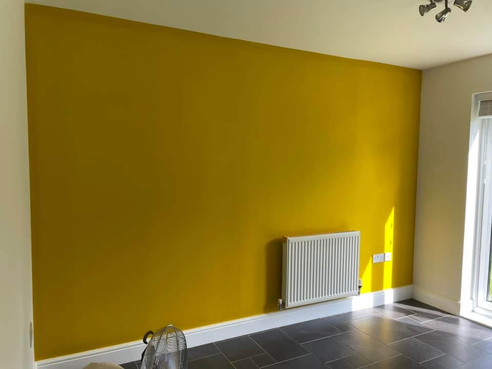 Yellow wall in a room with a radiator, window, and dark floor. Kitchen wall painted and decorated by Daffodil Decor in Swansea.