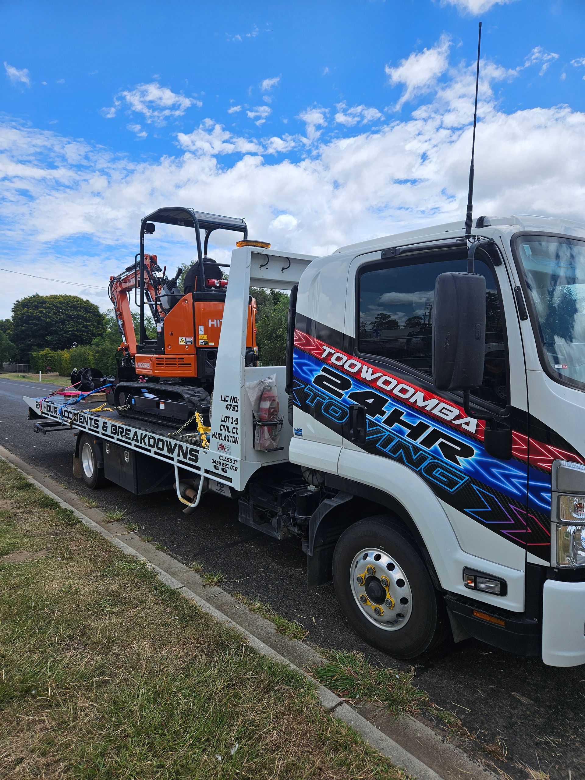 A white tow truck parked on a roadside, transporting an orange mini-excavator on its flatbed under a blue sky. — JP's Towing and Transport in Toowoomba City, QLD