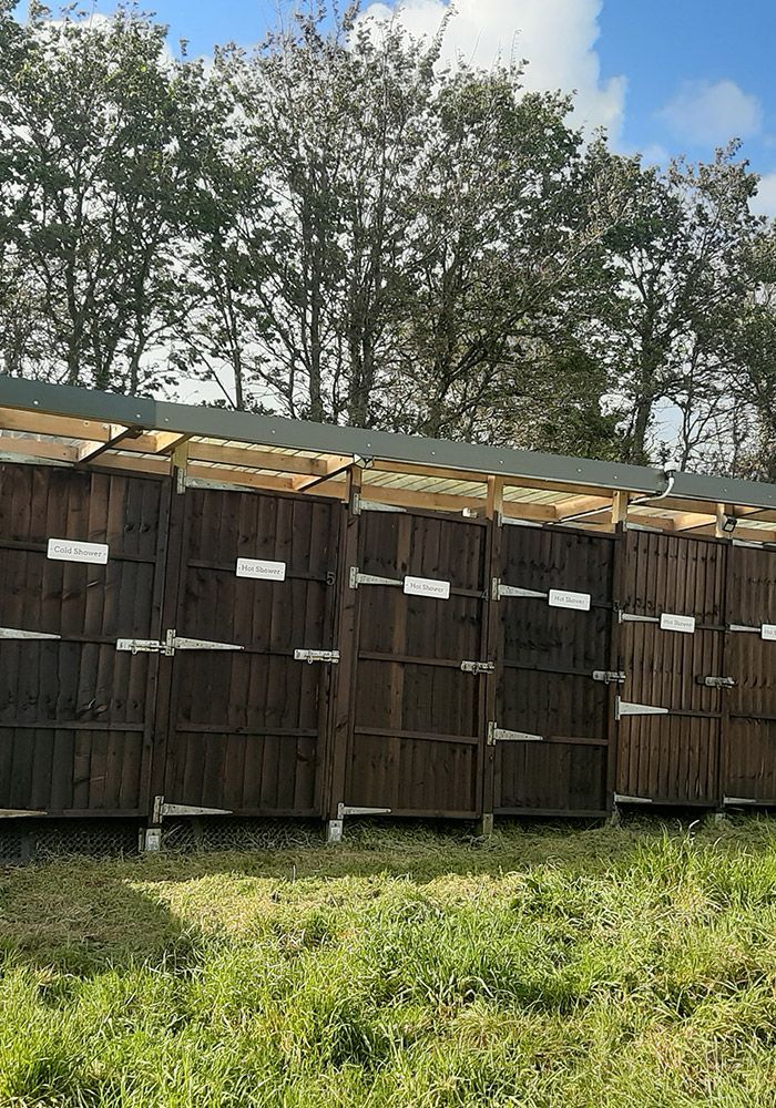 Wooden fence in a grassy field with trees in the background under a blue sky.