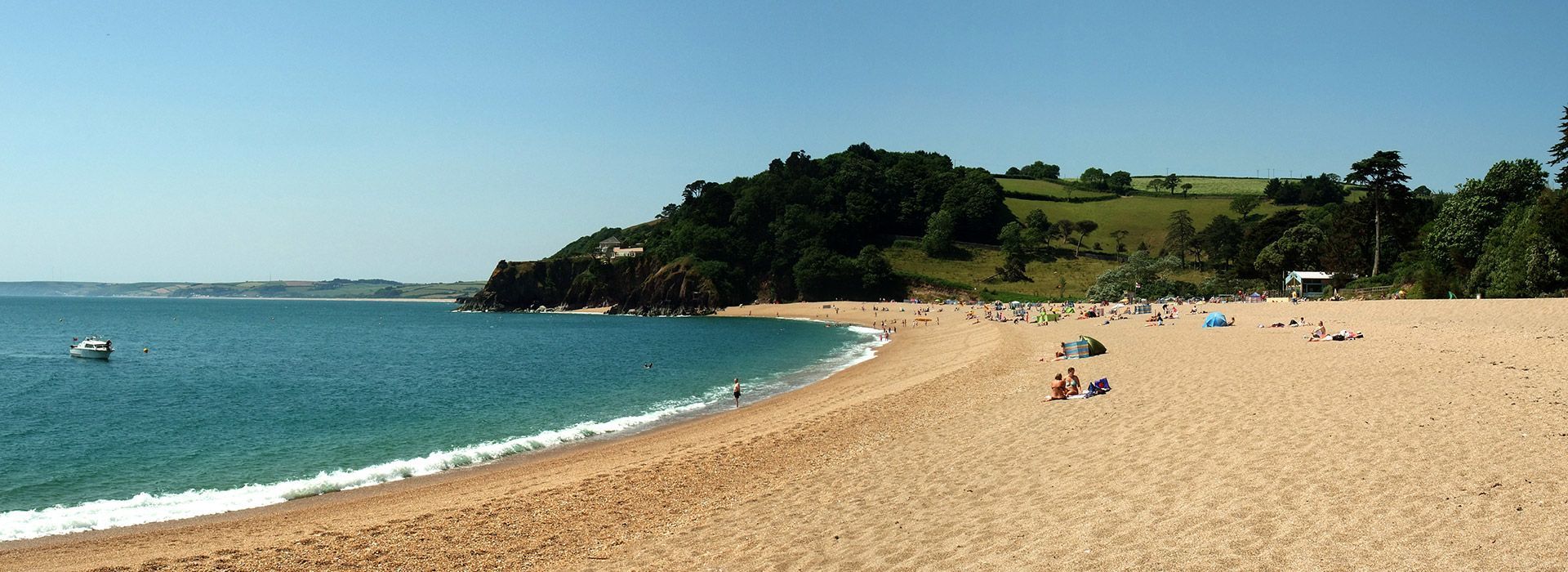Beach with sandy shore, turquoise water, trees, and people on a sunny day.