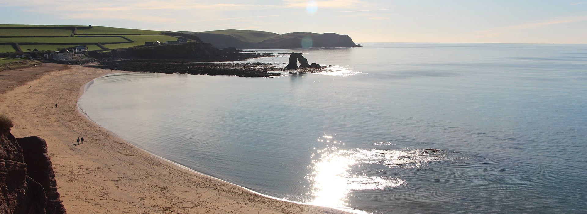 Sandy beach curving into a bay with cliffs and ocean under a bright sky.