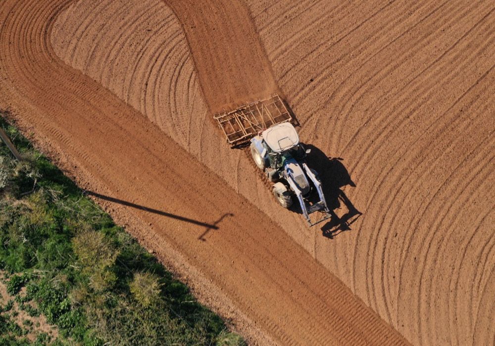 Tractor plowing a field, brown soil with curved lines. Overhead view, shadow of tractor.