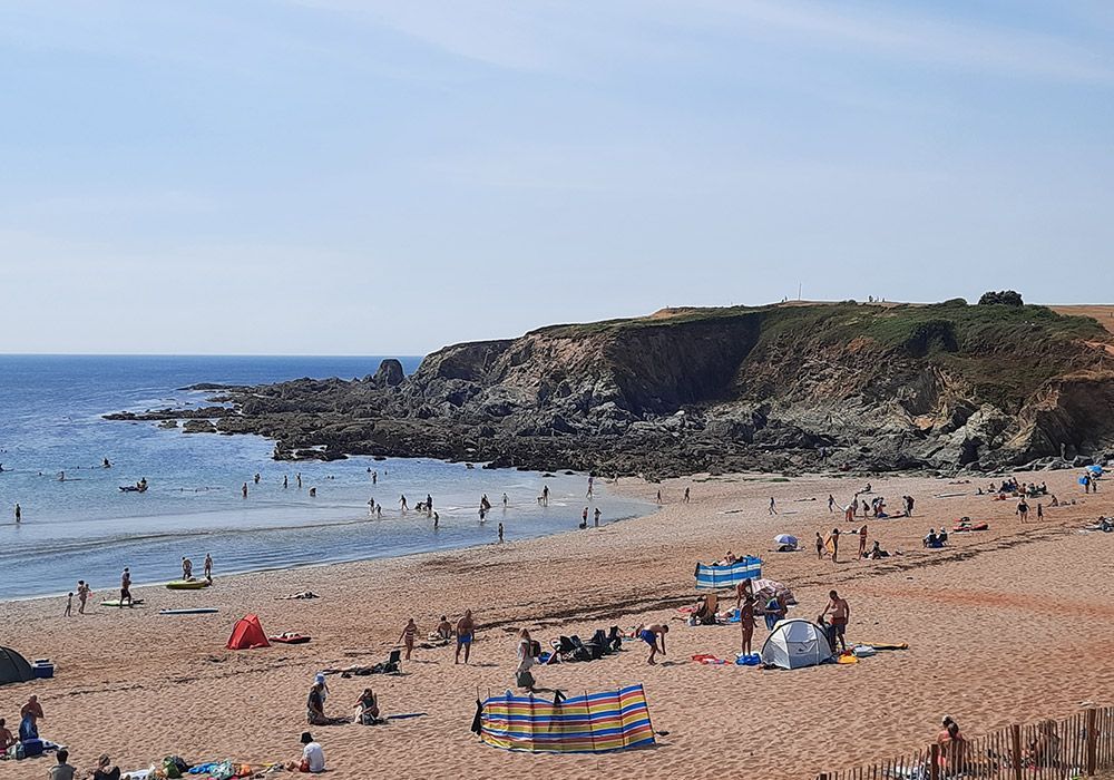 Beach scene with sand, people, and a rocky cliff under a clear sky.