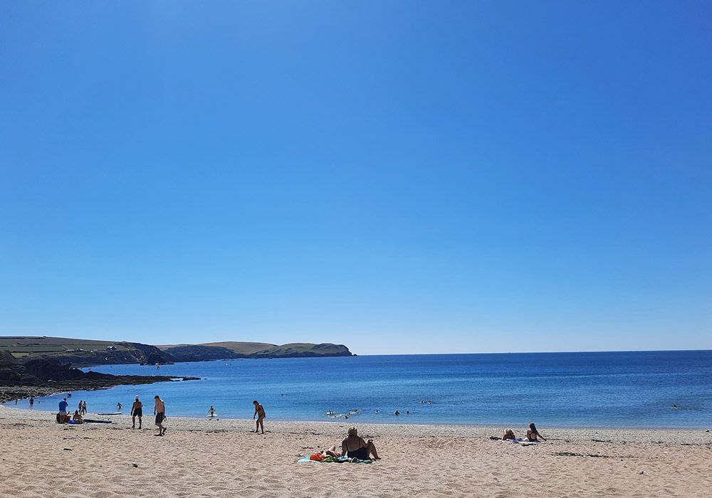 Beach scene with blue sky, ocean, sand, and people.