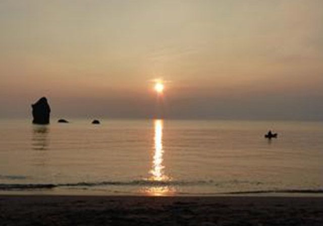 Sunset over ocean with solitary kayaker and rock formations.