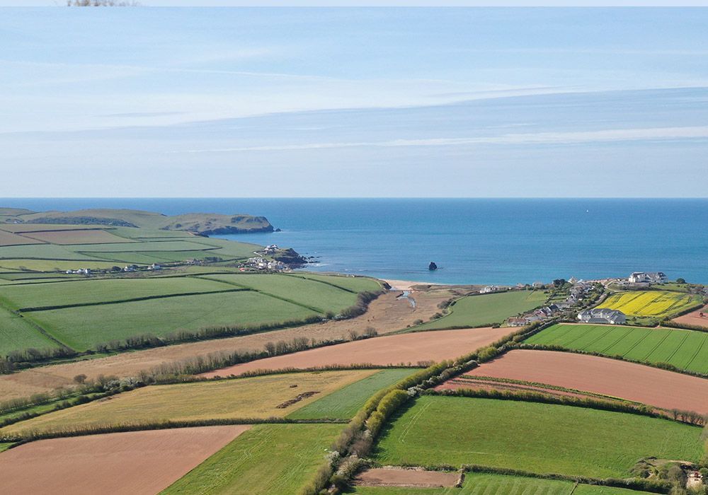 Rolling farmland meets coastline; green fields, blue ocean, sunny day.