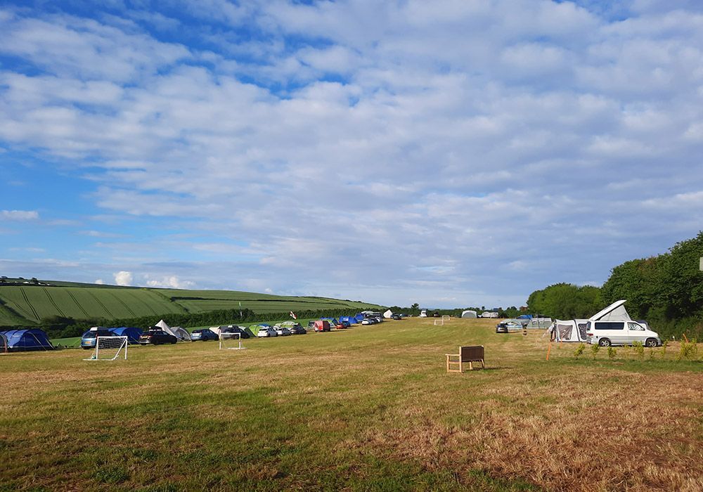 Camping field with tents, a campervan, and blue sky.