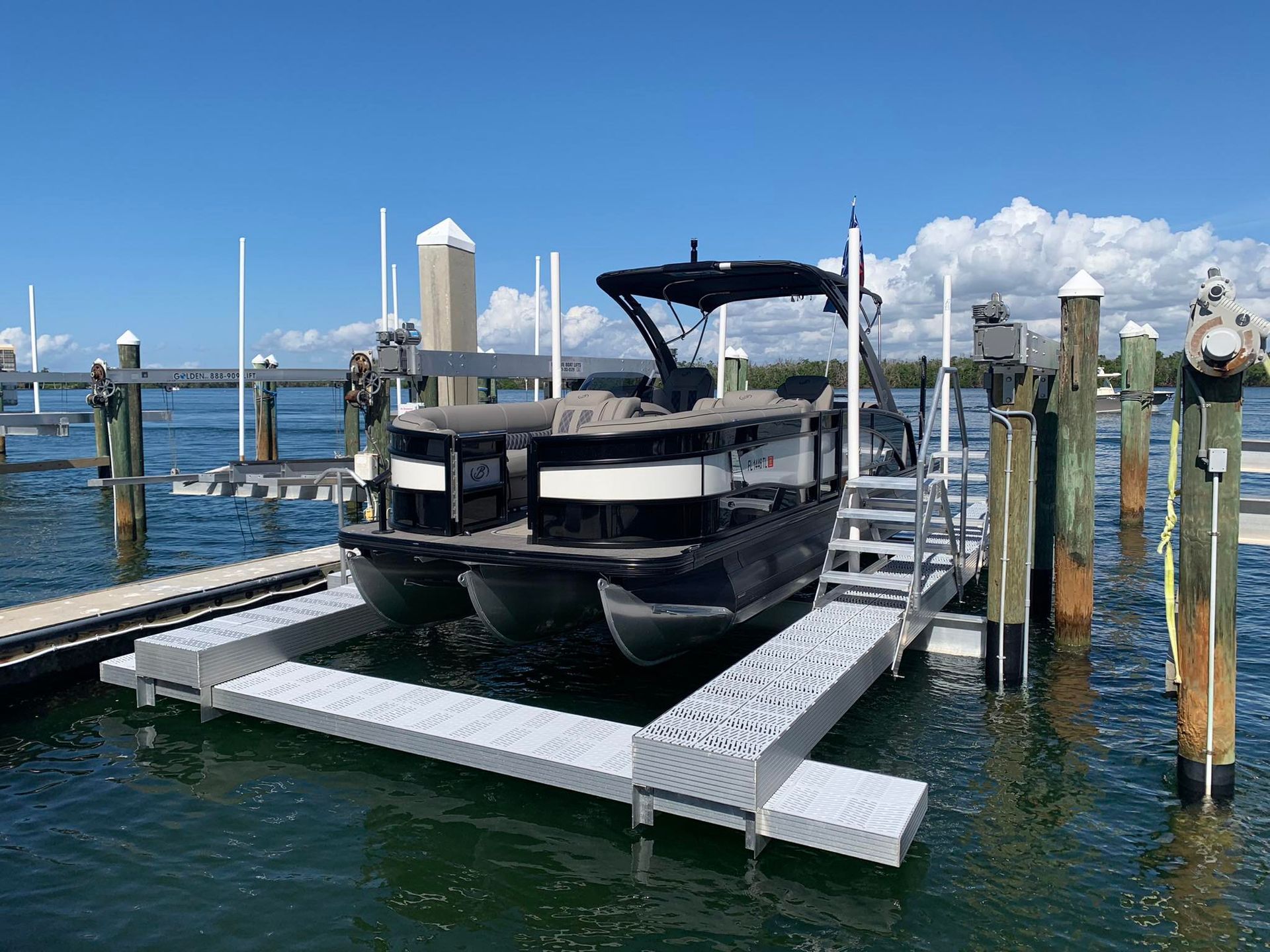 Black boat docked at a marina on a bright sunny day, with calm blue water and white docks.