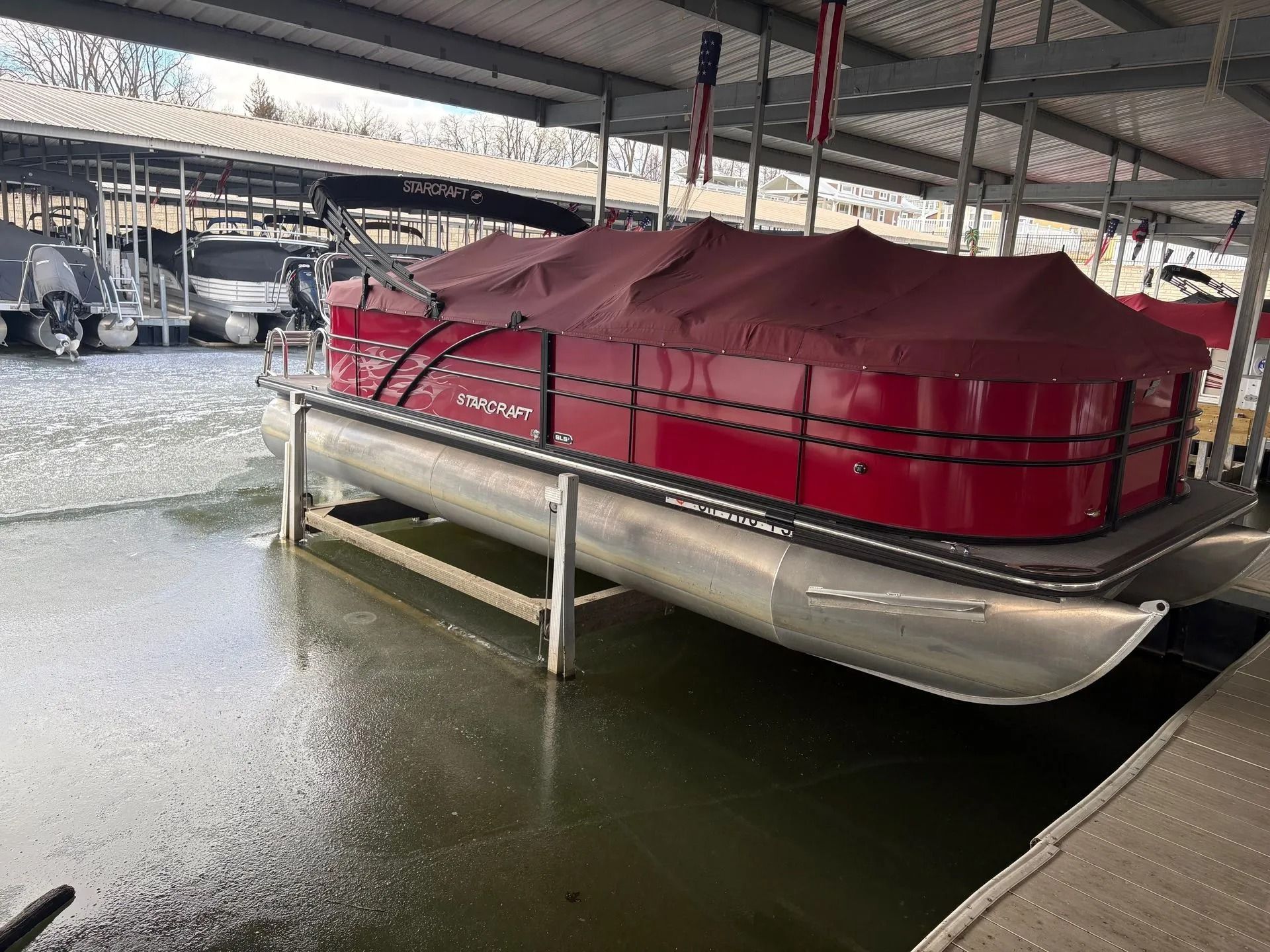 Red pontoon boat under a dock cover in a wet marina storage area