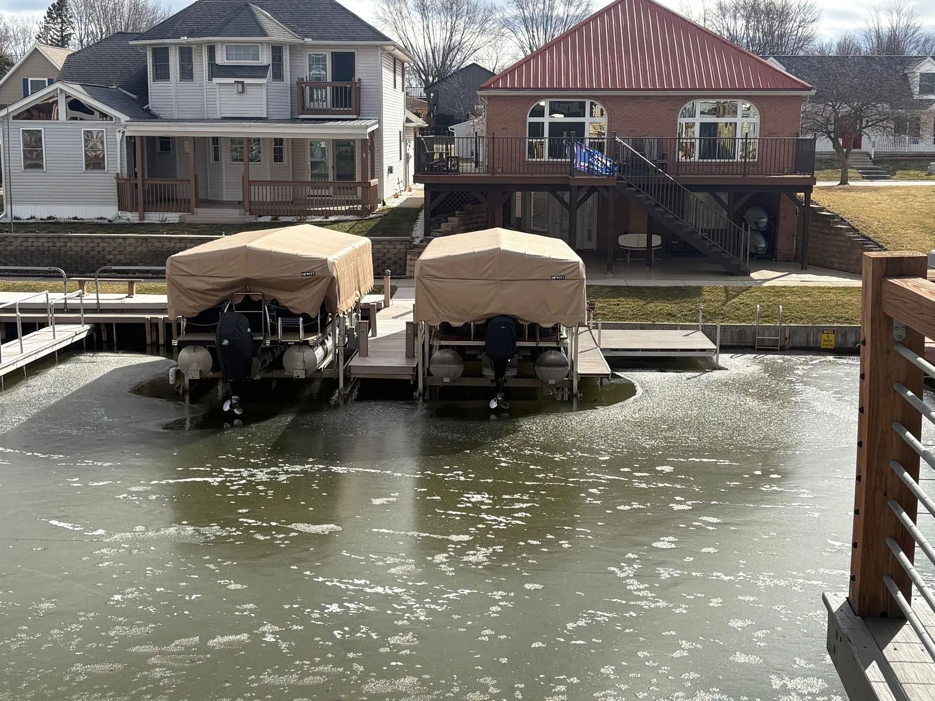 Two covered boats docked on a calm canal with waterfront homes in the background.