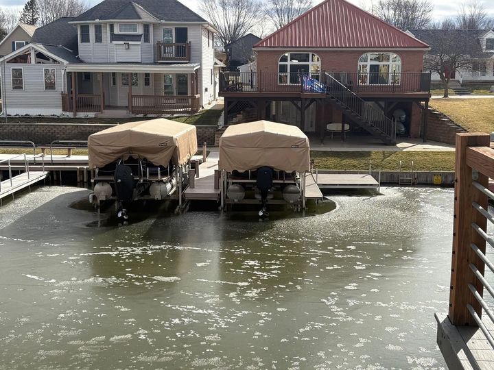 Two covered boats docked on a lake beside lakeside houses on a sunny day.