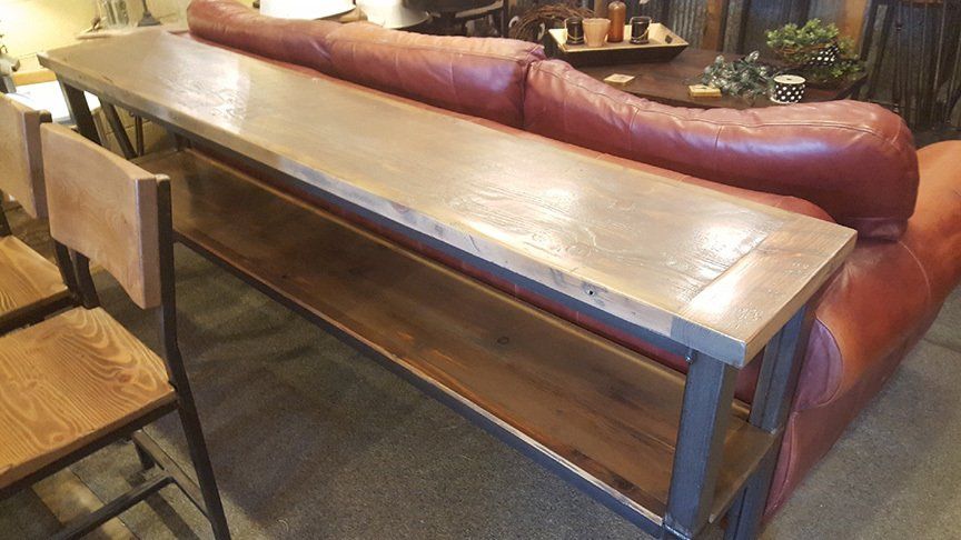 A long wooden table is sitting next to a red leather couch.