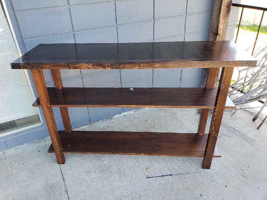 A wooden table with three shelves is sitting on a balcony.