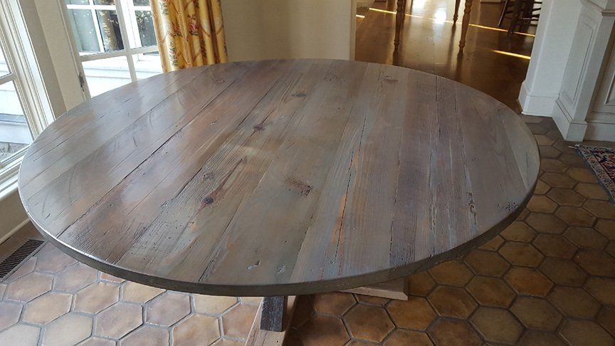 A round wooden table is sitting on a tiled floor in a room.