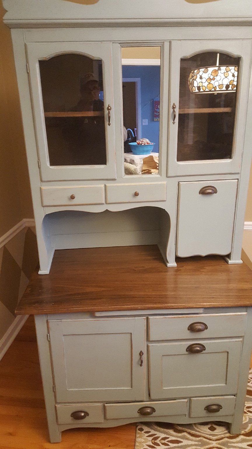 A white hutch with a wooden top and drawers is in a living room.