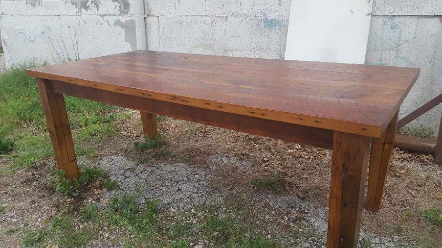 A wooden table is sitting in the grass in front of a concrete wall.
