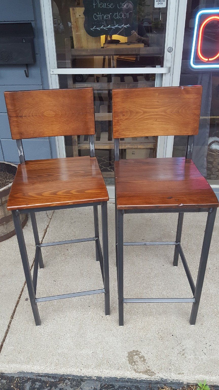Two wooden bar stools are sitting on a sidewalk in front of a store.