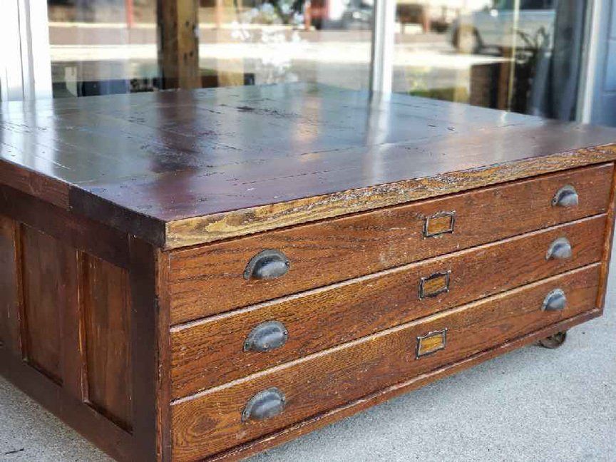 A wooden coffee table with three drawers and wheels.