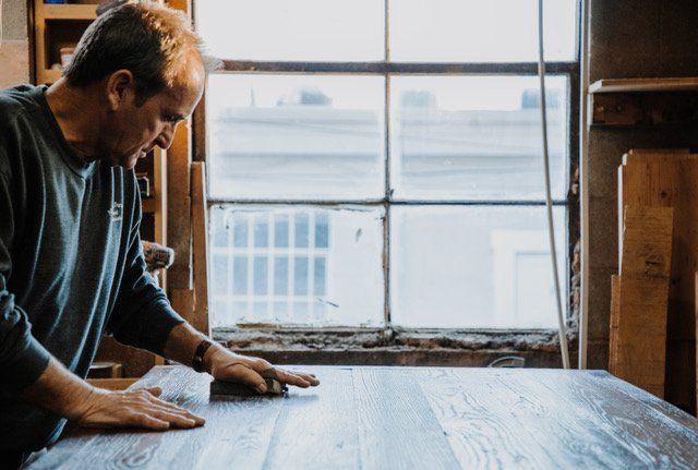 A man is working on a wooden table in front of a window.