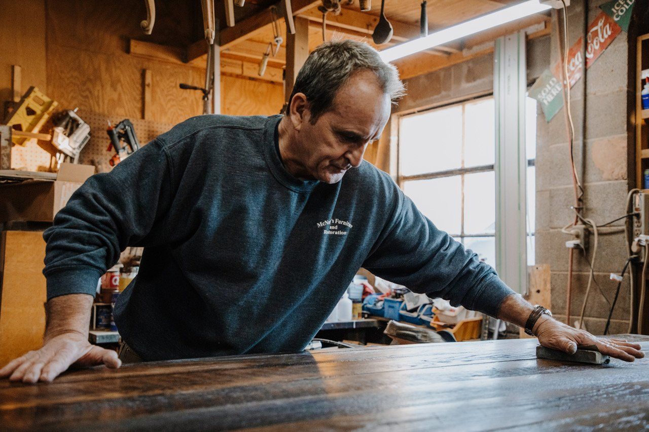 A man is working on a wooden table in a workshop.