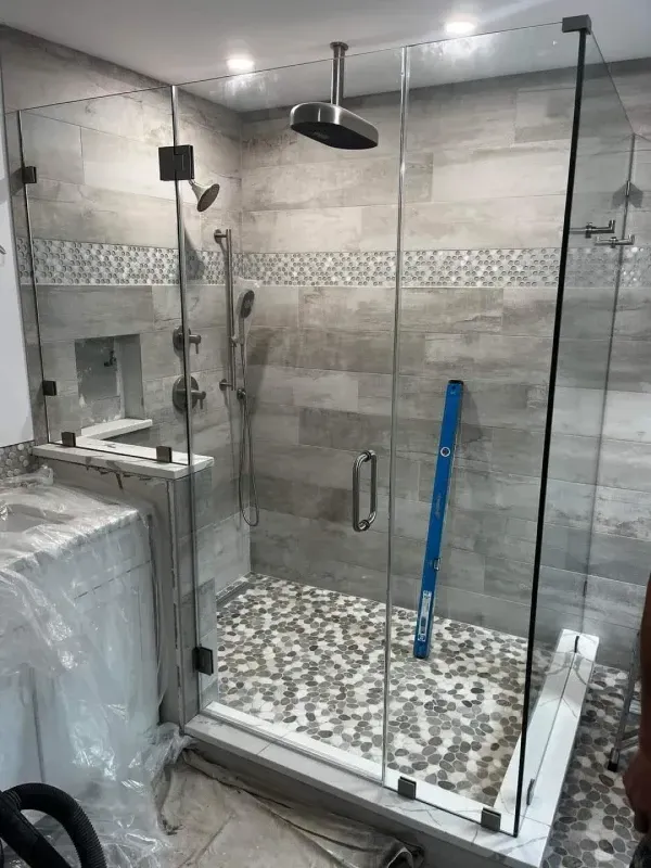 Glass shower enclosure with gray tile walls and pebble floor.