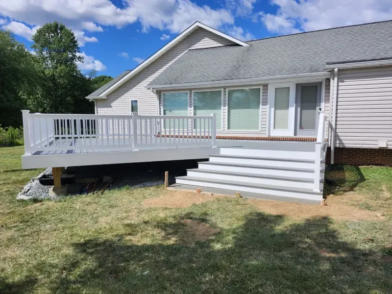 White deck and stairs lead to a house with a gray roof, surrounded by grass under a blue sky.