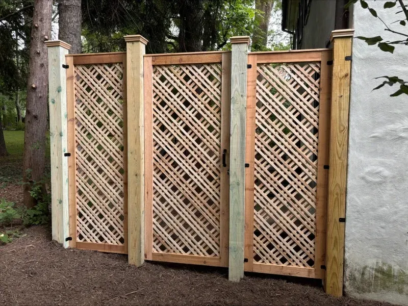 Wooden lattice fence with square posts, next to a tree and a stucco wall.