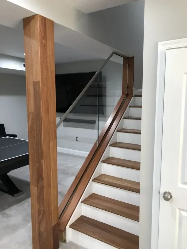 Staircase with wooden steps and railing, glass panels. Dark wood column, white walls, and a door on the right.