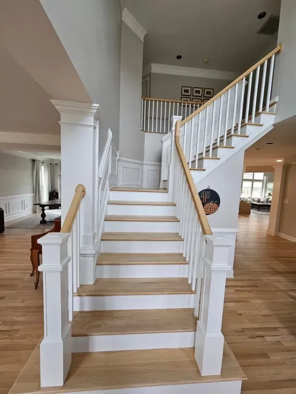 Two-story foyer with wooden staircase, white railing, and light wood flooring. Grey walls.
